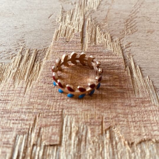 Bague anneau pour femme motif feuilles de laurier ciseles en acier inoxydable dore avec touches d email rouge bordeaux et bleu pose sur bois