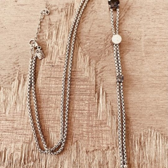 Collier en acier inoxydable maille rombo à pendentif coulissant, pierre bleu azur et fermoir mousqueton, posé sur bois