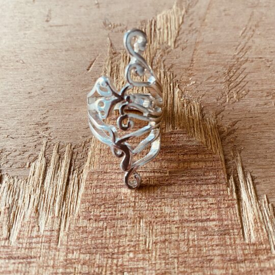 Bague en acier motif arabesque ajouré, posée sur bois
