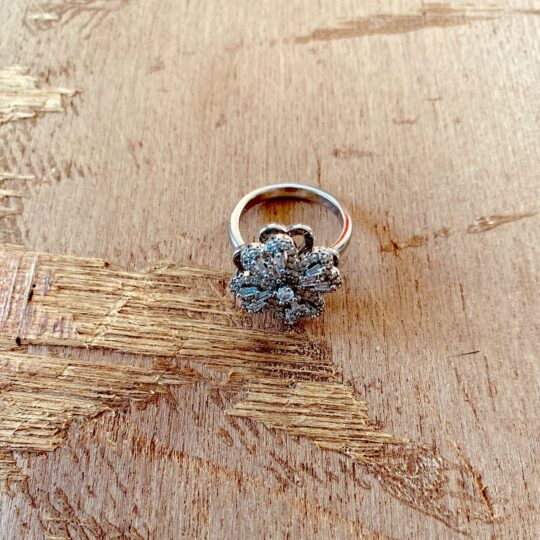 Bague argentée en forme de fleur sertie de zircons avec cœur ajouré, posée sur bois